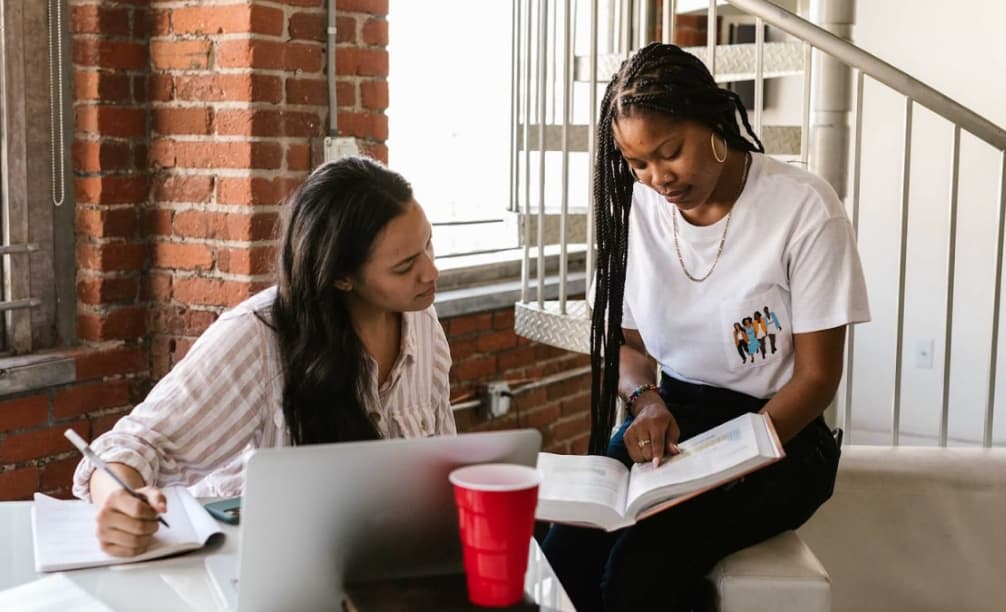 Two women studying together, one with a laptop and the other with a book