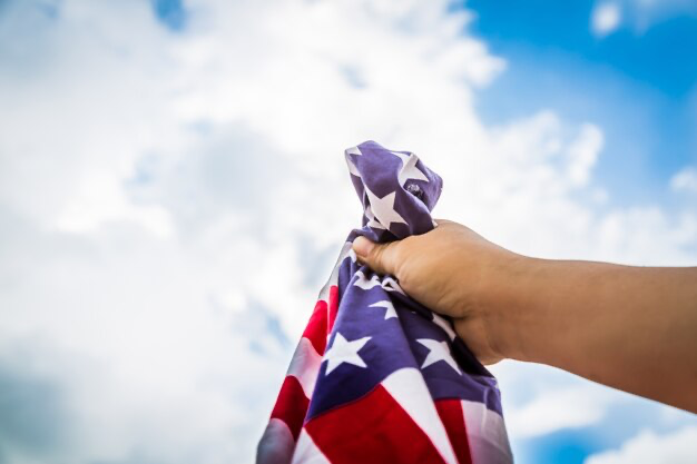 Hand holding American flag against sky